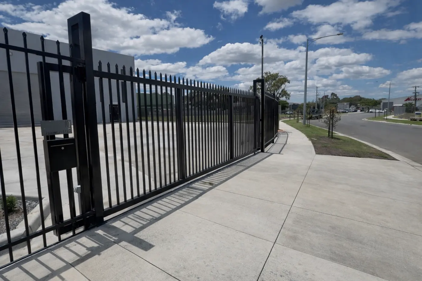 Black spear-top steel sliding gate closed across a wide concrete driveway, with matching fence beside it